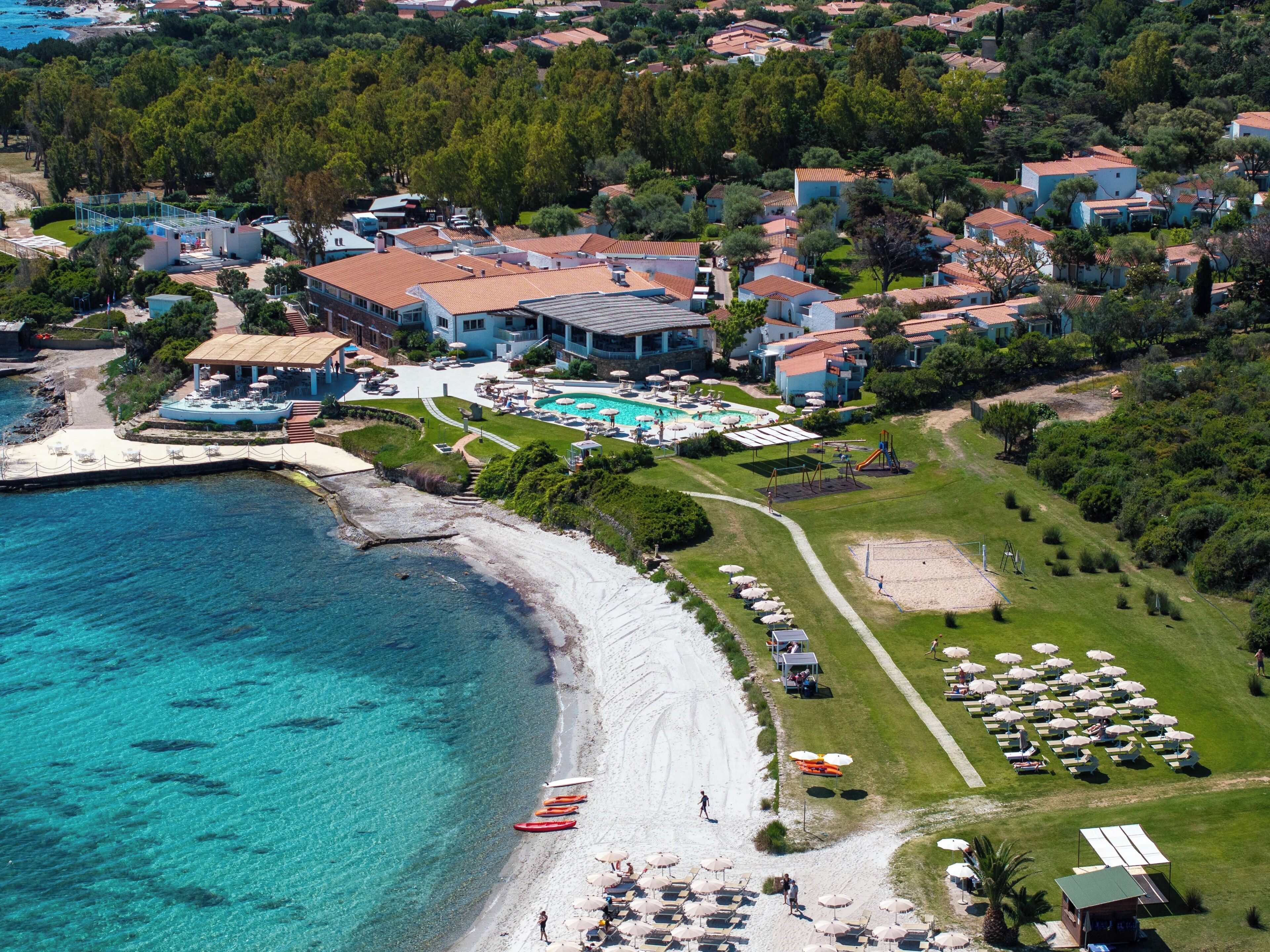 An aerial view of a coastal resort with a beach, swimming pool, and multiple villas.