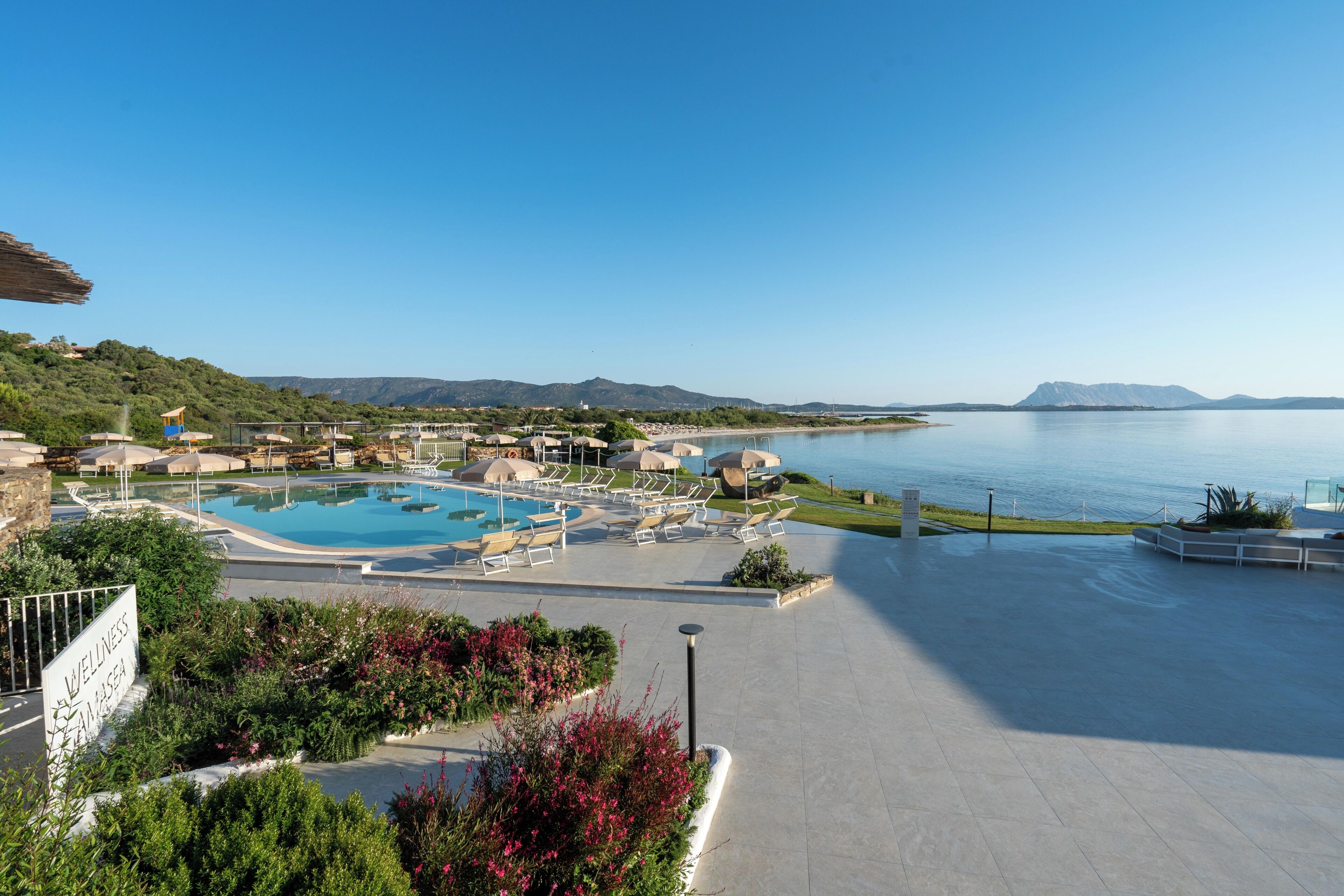 Un resort con una piscina grande, zonas de descanso y vista al mar.