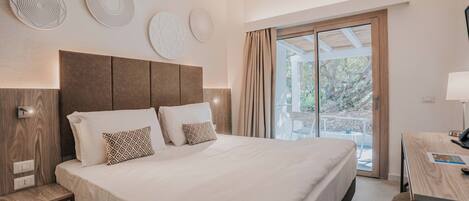 Een moderne hotelkamer met een groot bed, een bureau en een balkon met uitzicht op bomen.