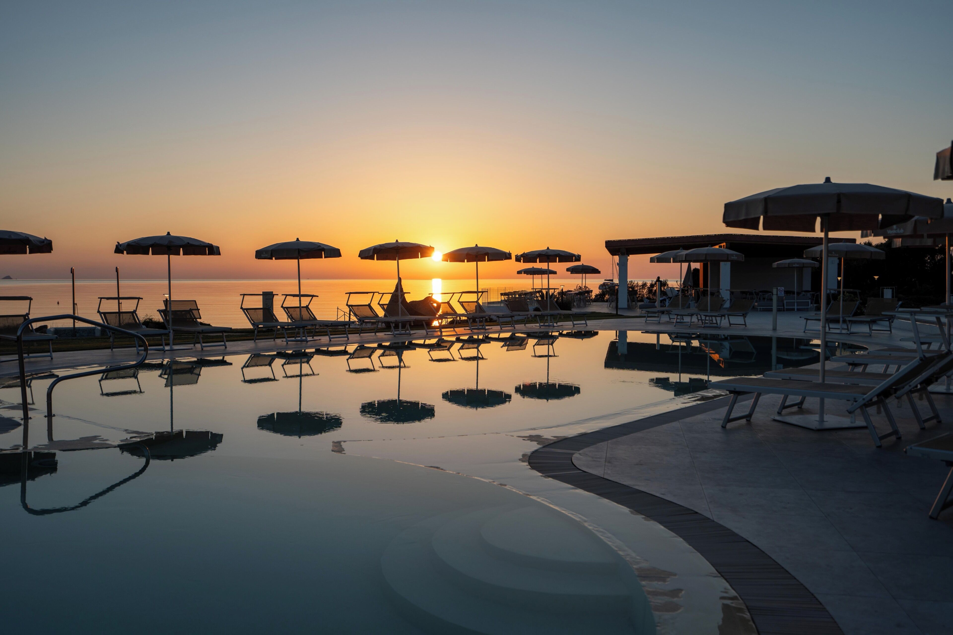 A poolside area with lounge chairs and umbrellas, a clear sky, and a sunset.