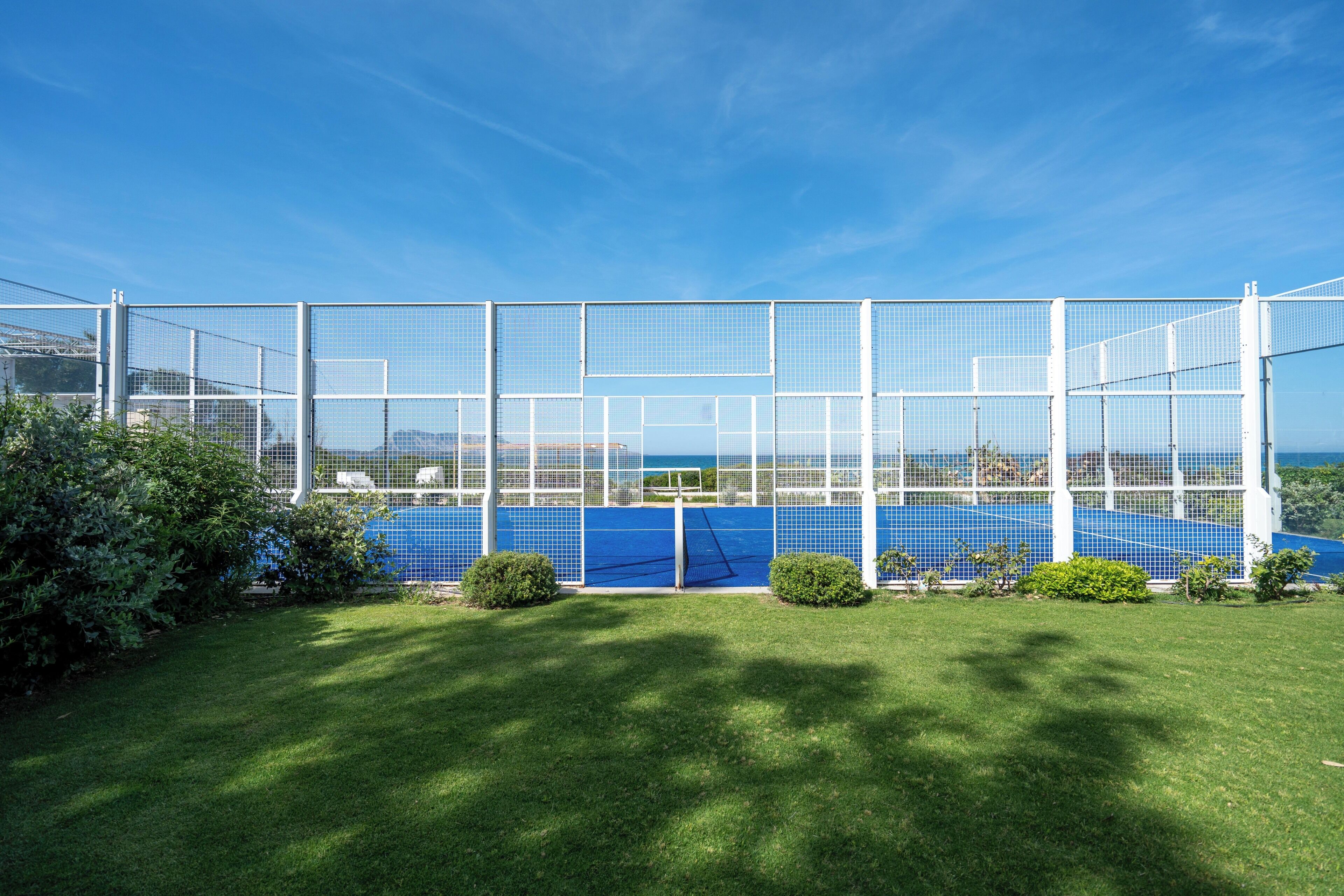 Una cancha de tenis rodeada por una cerca blanca, con un cielo azul despejado.