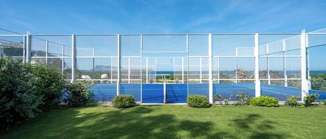 Una cancha de tenis rodeada por una cerca blanca, con un cielo azul despejado.