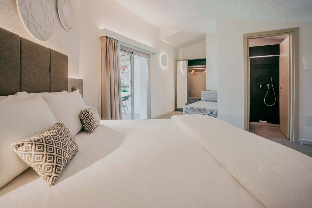 A modern hotel room with a large bed, a walk-in closet, and a shower area.