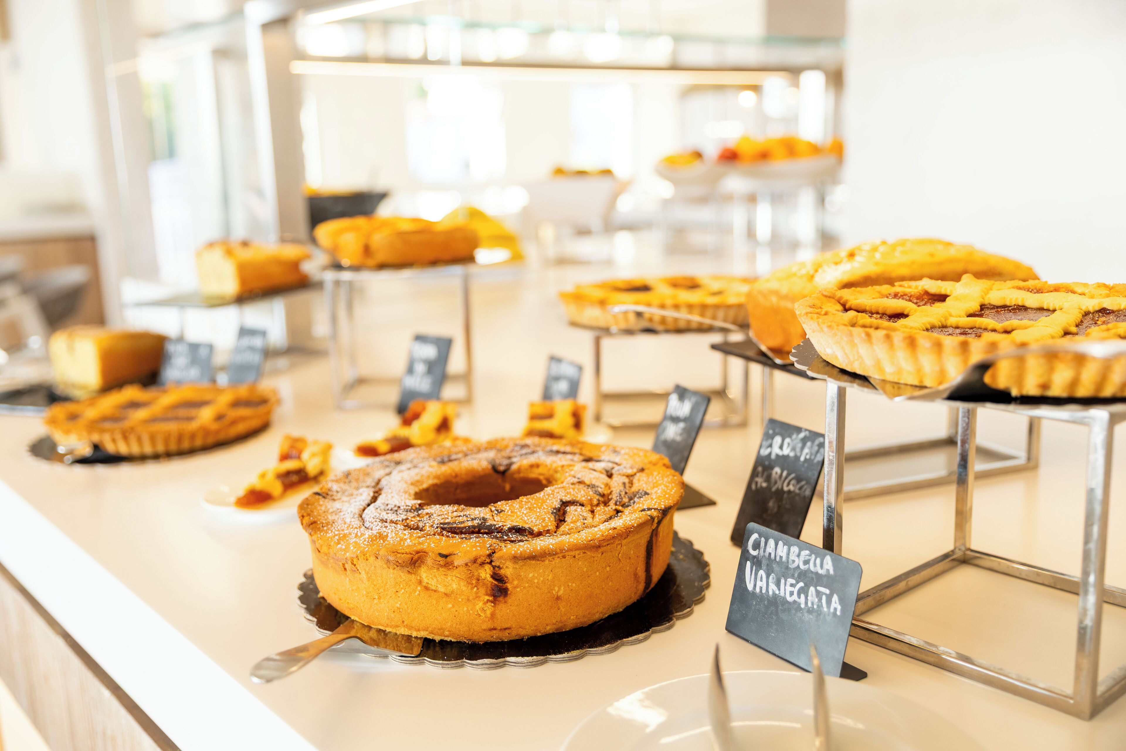 Een bakkerijvitrine met diverse taarten en gebak, waaronder een kaneelwhoreltaart en een chocoladetaart.