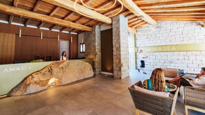 A reception area with a stone counter, wooden ceiling beams, and wicker furniture. - Amasea Resort (San Teodoro)