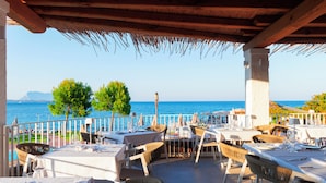 An outdoor dining area with tables and chairs, overlooking a body of water. - Amasea Resort (San Teodoro)