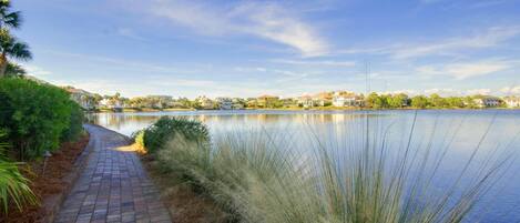 A paved pathway beside a calm lake with houses in the background.