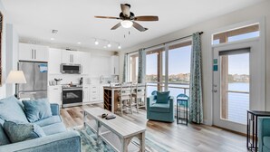A modern apartment with a kitchenette, dining area, and a large window overlooking a body of water. - Destiny Beach Villas #15a&b (Destin)