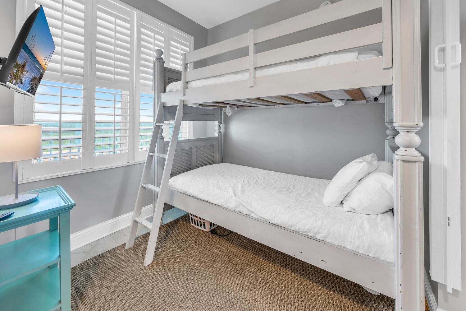 Habitación con literas, un escritorio con lámpara y vista al exterior por la ventana.