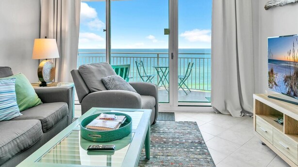 Un balcon avec vue sur la mer, un canapé, une table basse et un téléviseur posé sur un meuble.
