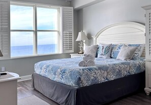 Relax in this serene bedroom with a large bed, white nightstand, and dresser, offering a stunning ocean view.
