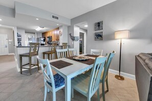Enjoy meals in this stylish dining area with a table for four, featuring comfortable chairs and a modern kitchen in the background.