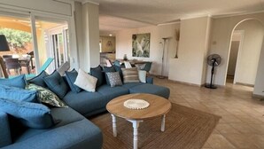 Ein geräumiges Wohnzimmer mit einem blauen Ecksofa, einem runden Couchtisch und einem großen Fenster, das für natürliches Licht sorgt.