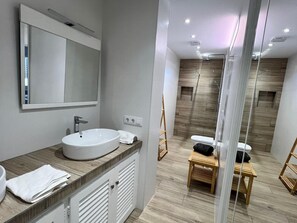 A modern bathroom with a large mirror, a round sink, and a shower area.