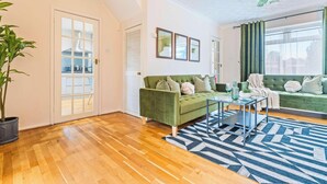 A modern living room with a green sofa, a glass coffee table, and a large window with curtains.
