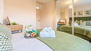 A hotel room with two beds, a wooden headboard, a mirror, and a tray with towels and snacks.