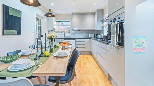 A modern kitchen with a dining area, equipped with stainless steel appliances, a large window, and a dining table set for six.