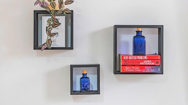 Three framed items on a wall: a framed botanical illustration, a framed book titled 'Very British Problems' by James Patterson, and a framed blue bottle. - Family & Contractor Friendly Stay | WiFi, Parking (Farnborough)
