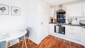 Een moderne keuken met witte kastjes, een fornuis en een eethoek met een witte tafel en stoelen.