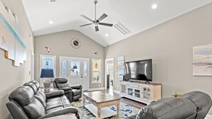 A spacious living room with a ceiling fan, leather sofas, a coffee table, and a TV on a cabinet.