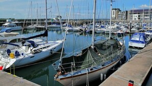 Un port de plaisance où sont amarrés de nombreux bateaux, un ciel dégagé et des bâtiments en arrière-plan.