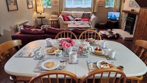 A cozy dining area with a round table set for four, surrounded by wooden chairs. A floral centerpiece and various dishes are on the table.