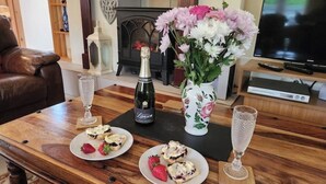 A wooden table with two plates of pastries, a bottle of champagne, and a vase with flowers.