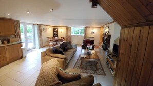 A spacious living room with a sofa, coffee table, and fireplace. There is a dining area with a table and chairs, and a kitchen with wooden cabinets.
