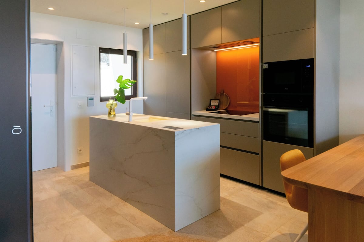 Una cocina moderna con una isla central, electrodomésticos integrados y un comedor con mesa y sillas de madera.