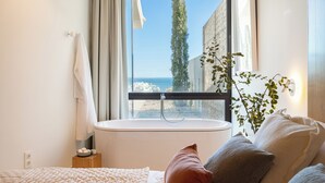 A modern bathroom with a bathtub, a window with a view of the sea, and a plant. - Leiro Residences - Preferred Hotels & Resorts (Fuengirola)