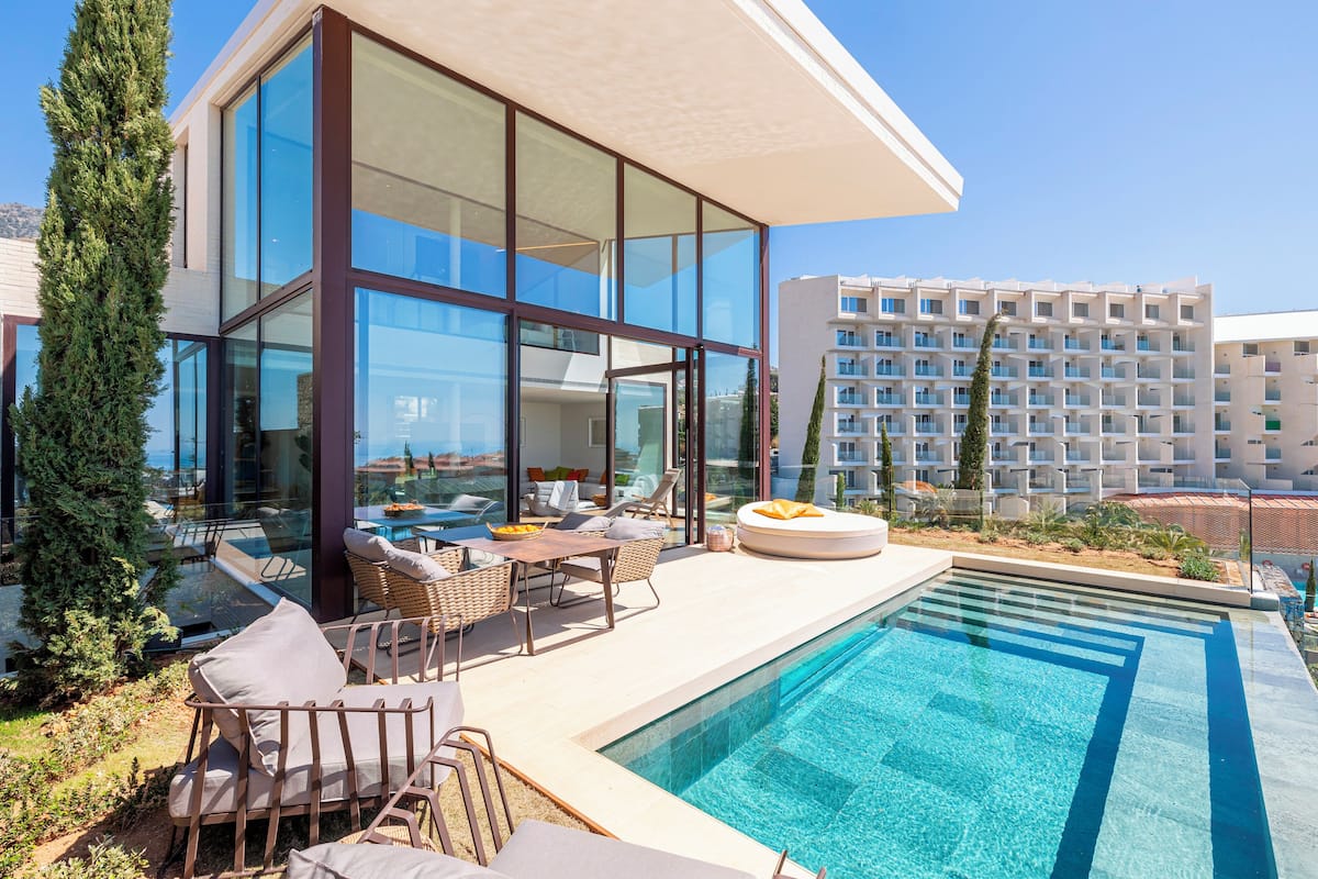 Un hotel moderno con zona de piscina cubierta de cristal, asientos exteriores y vistas a la ciudad.