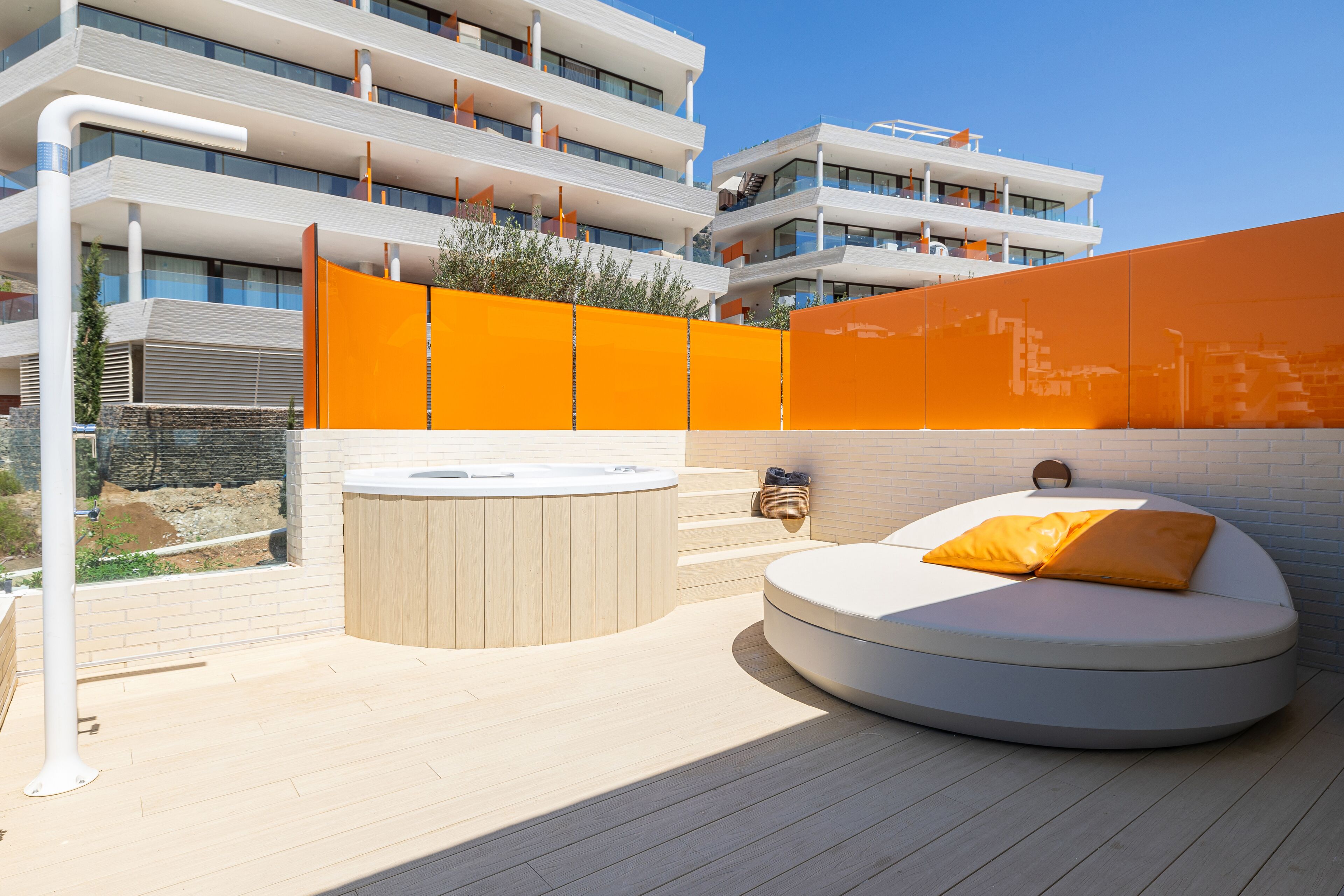 Un espacio exterior moderno para relajarse, con un jacuzzi, una zona de estar circular con cojines y vista a un edificio de varios pisos.