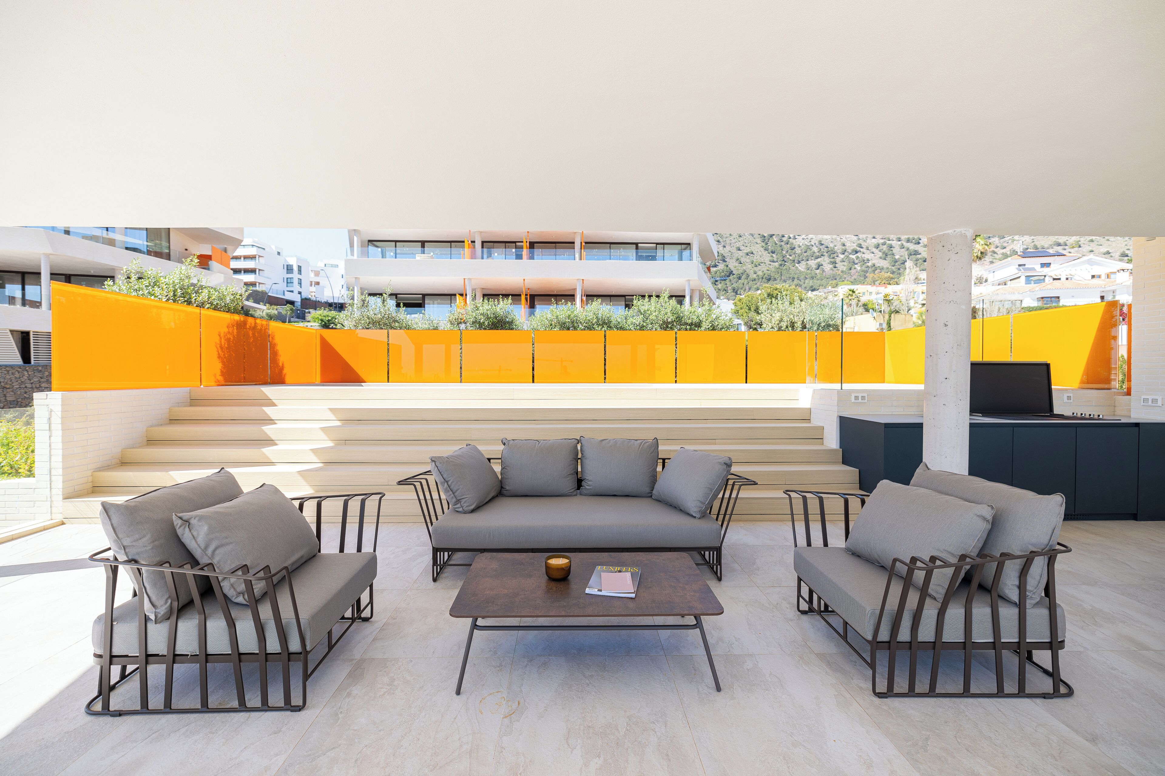 A modern outdoor seating area with a sofa and armchairs, a coffee table, and a view of a building and steps in the background.