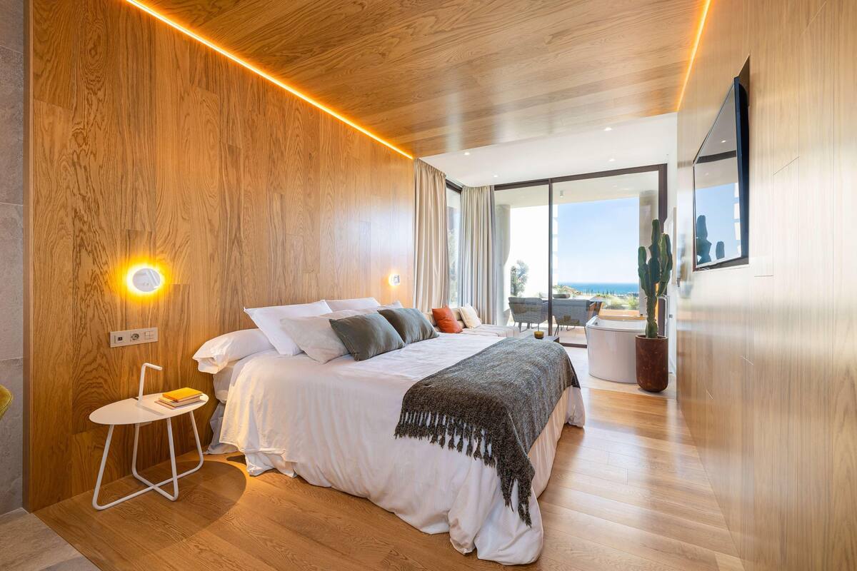 Un dormitorio moderno con una cama grande, mesitas de noche, vistas al exterior y una pared de madera.