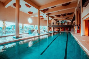 An indoor swimming pool with clear water, surrounded by white columns and a view of the city.