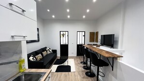 A modern kitchen with a black countertop, a sink, and a wooden dining table with black chairs. - Urban Flat 01 - Charming 2 bedroom Flat in Montorgueil (París)