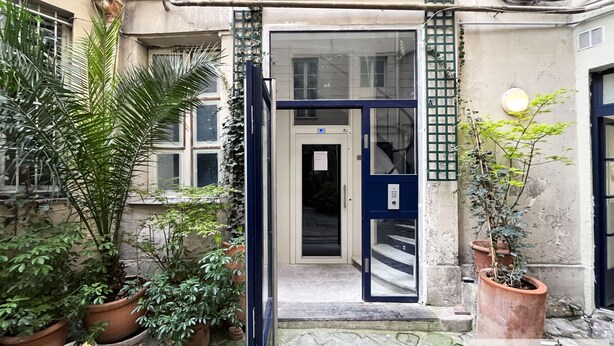 A building entrance with a glass door, potted plants, and a small outdoor area. - Urban Flat 01 - Charming 2 bedroom Flat in Montorgueil (París)