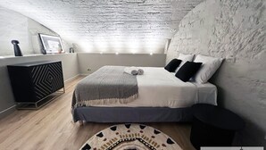 A modern bedroom with a sloped ceiling, a bed with white bedding, a patterned throw, and a decorative rug. - Urban Flat 01 - Charming 2 bedroom Flat in Montorgueil (París)