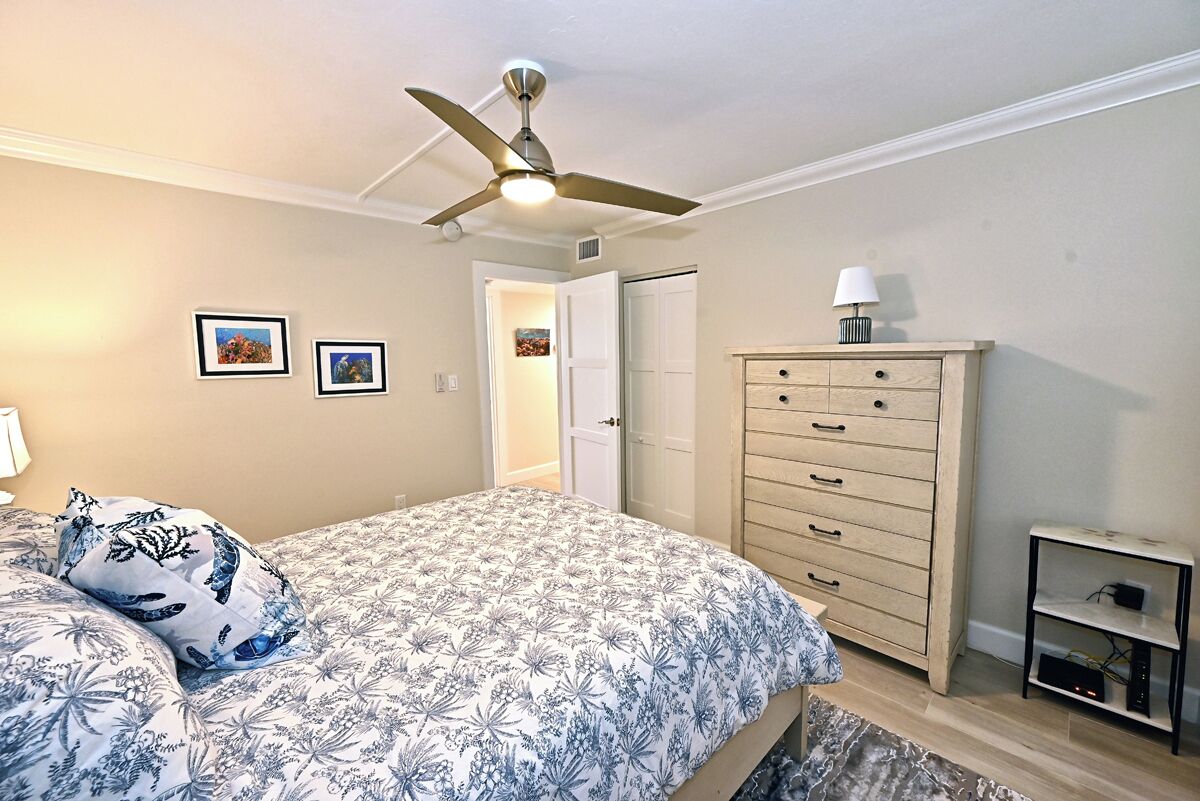 A bedroom with a bed, a ceiling fan, a dresser, and a door leading to another room.
