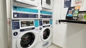 A laundry facility with multiple washing machines and dryers, labeled with usage instructions and capacity information.