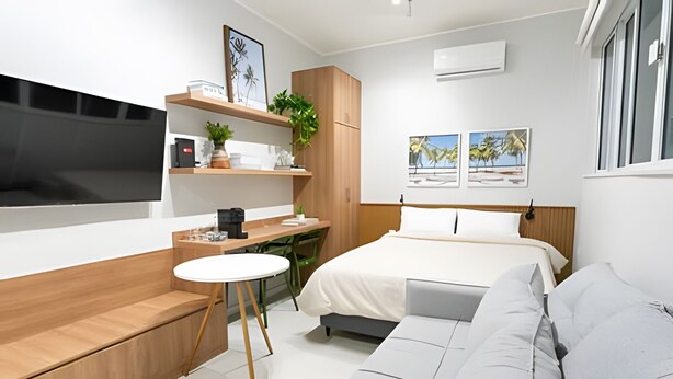A modern hotel room with a bed, a sofa, a desk, and a TV.