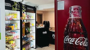 A store interior with shelves stocked with various products, a Coca-Cola refrigerator, and a freezer in the foreground.