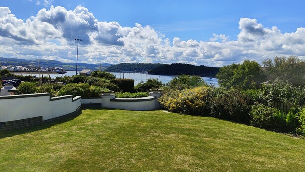 A grassy area with a white building, a view of a lake with boats, and a hilly landscape in the distance. - Riverside Retreat - One Bedroom Cottage, Sleeps 2 (Deganwy)
