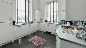 A modern kitchen with white cabinets, a gas stove, and a window with blinds. - Riverside Retreat - One Bedroom Cottage, Sleeps 2 (Deganwy)
