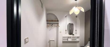 Une chambre à coucher moderne avec un lit, un miroir, un luminaire suspendu et une petite étagère sur laquelle est posée une plante.