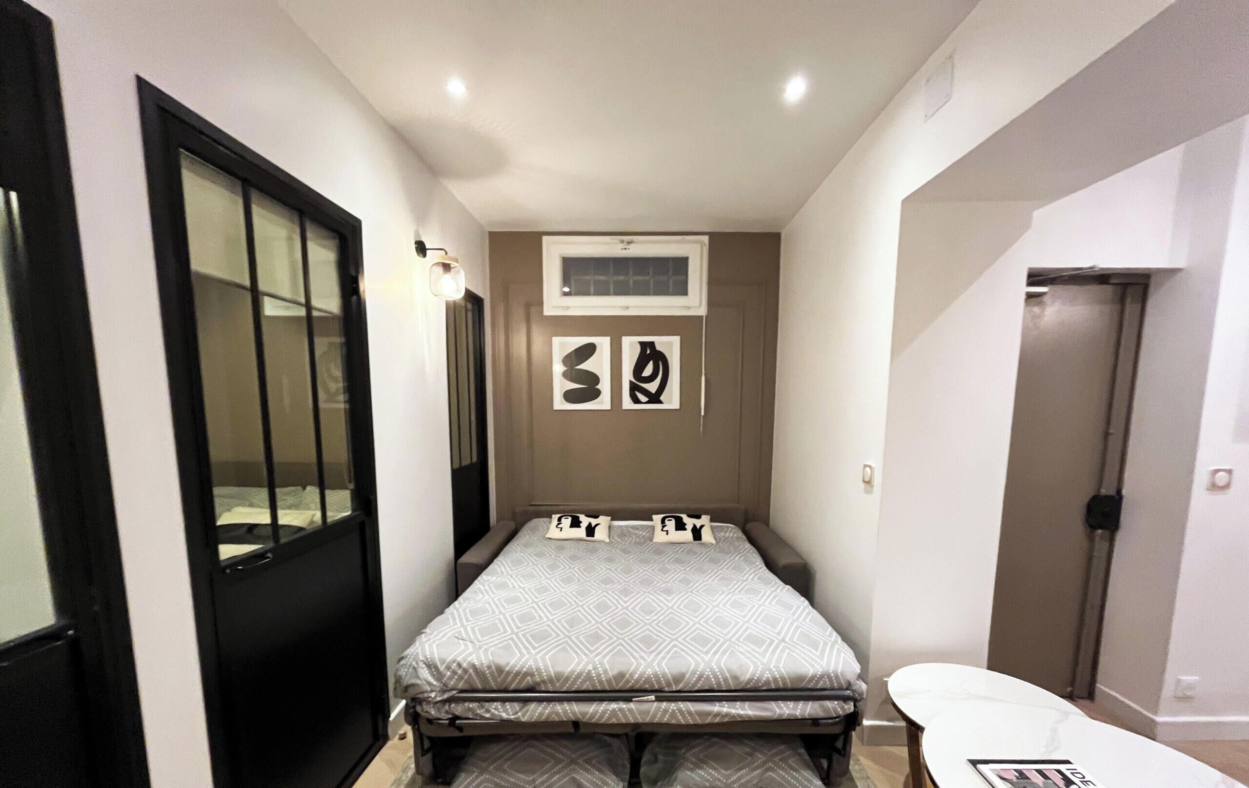 A compact bedroom with a bed, a small table, and a door.
