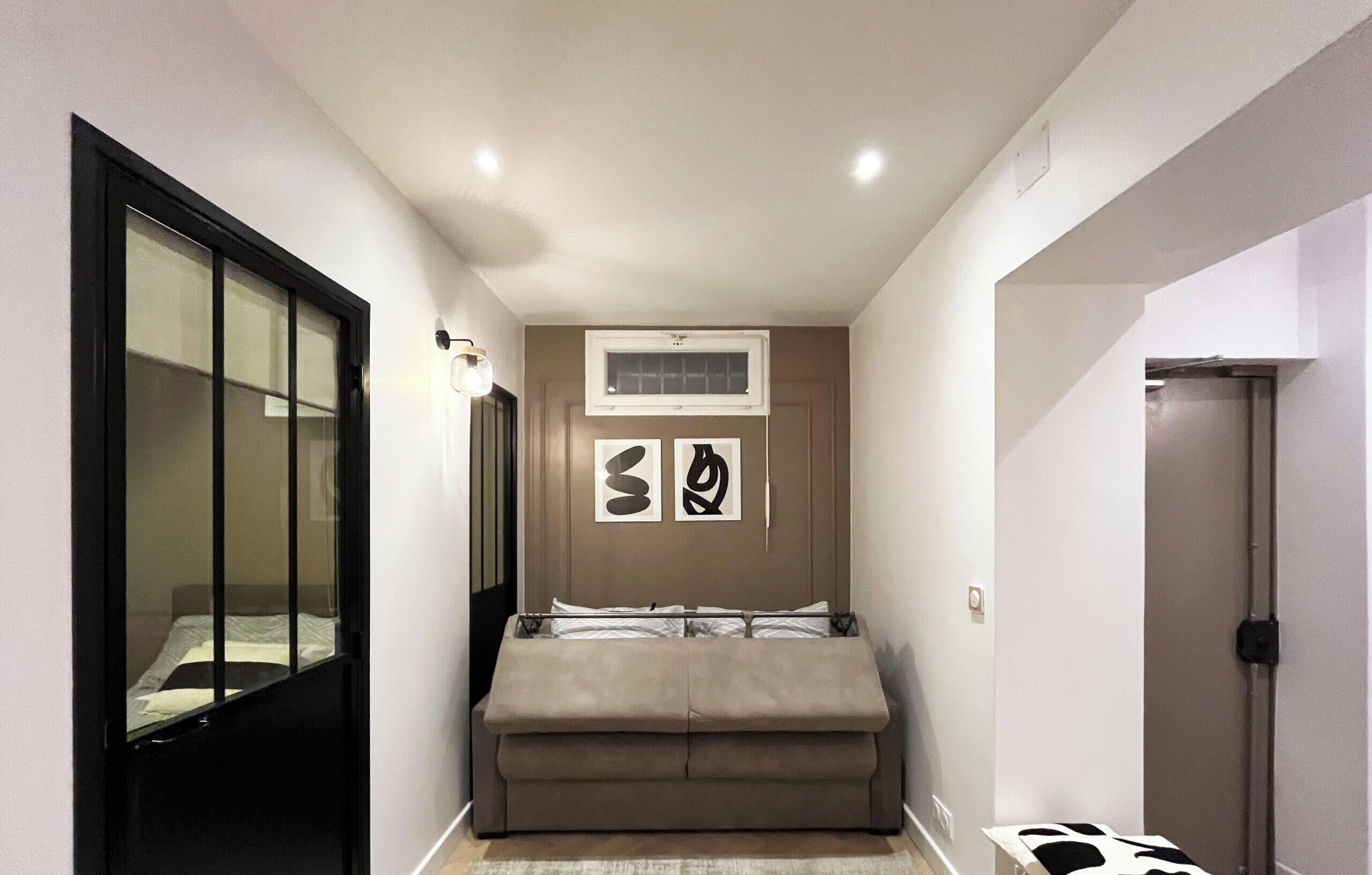 A narrow hallway with a bed, a large window, and a door.