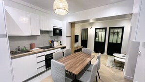 A modern kitchen with white cabinets, a wooden dining table, and a hanging light fixture. - Urban Flat 178 - Newly Renovated 2 BDR Flat in Paris (Paris)