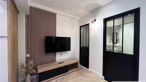 A modern hallway with a flat-screen TV mounted on a wooden panel, a glass door with a black frame, and a light fixture on the wall. - Urban Flat 178 - Newly Renovated 2 BDR Flat in Paris (Paris)