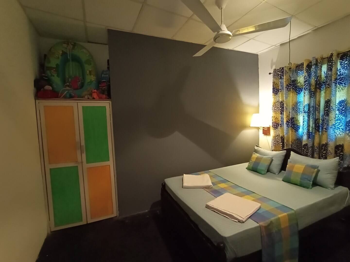 Ein Schlafzimmer mit Bett, Kissen, Deckenventilator, Kleiderschrank und Vorhängen.